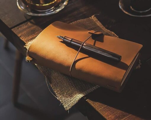 gammaldags läder anteckningsbok ligger på ett bord. Ovanpå boken ligger en reservoarpenna.
